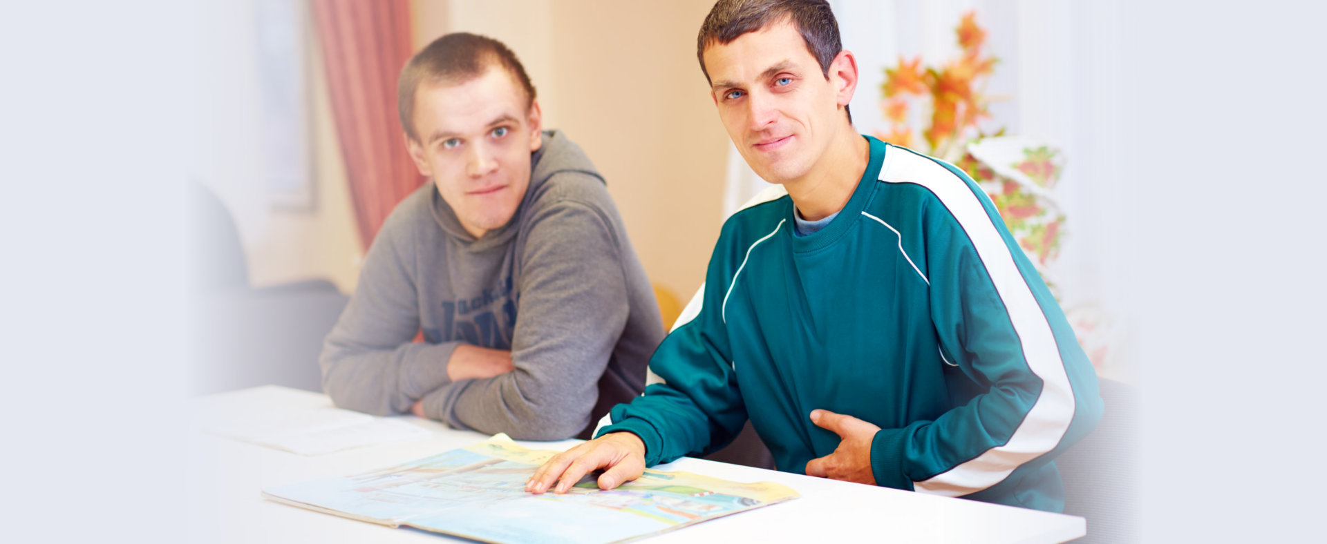 cheerful adult men with disability sitting at the desk in rehabilitation center